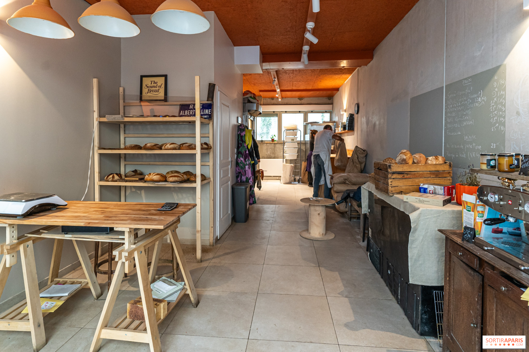L'intérieur de La Boulangerie Nouvelle: étagères en pin garnies de pains au levain, table à tréteaux et ardoise des prix