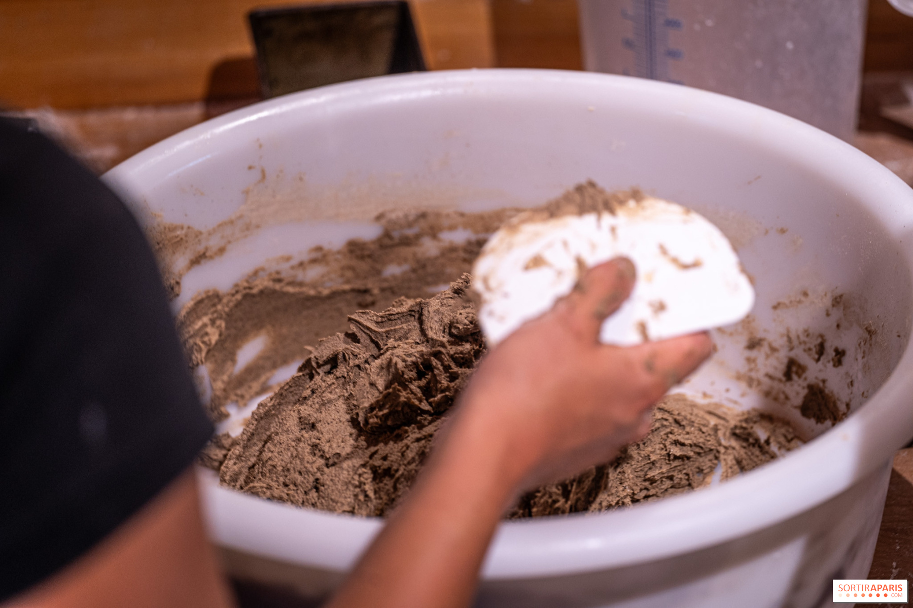 Les mains de Clément travaillant une pâte hydratée de blés anciens dans un bac
